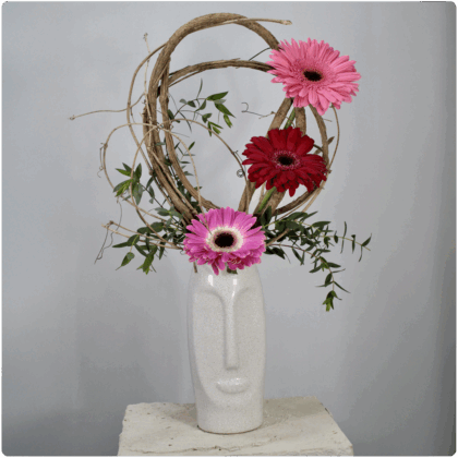 Arreglo de gerberas con detalles de bejuco y follaje con base de cerámica en forma de rostro