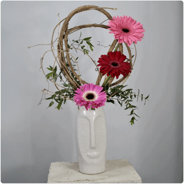 Arreglo de gerberas con detalles de bejuco y follaje con base de cerámica en forma de rostro